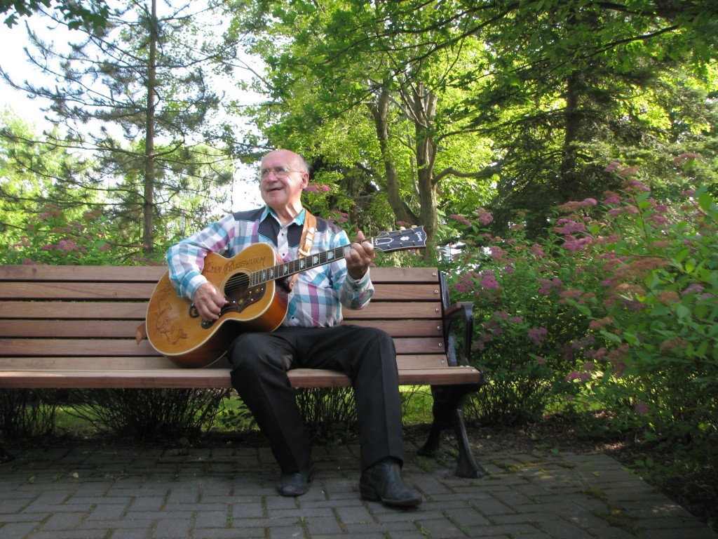 Lynn Russwurm holds his custom woodburned guitar as he sits on a bench in Gore Park, Elmira